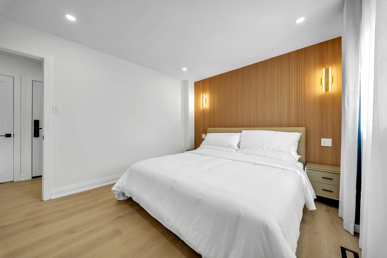 Bedroom with a white bed, wood accent wall, and warm wall lights.