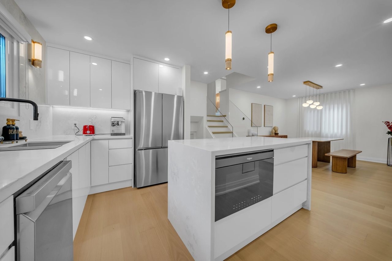 White kitchen with an island, pendant lighting, and stainless steel appliances.